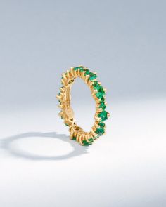 a gold ring with green stones on the inside and outside, set against a white background