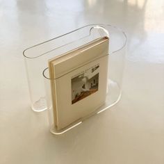 an open book sitting on top of a white table next to a glass container with a photo inside