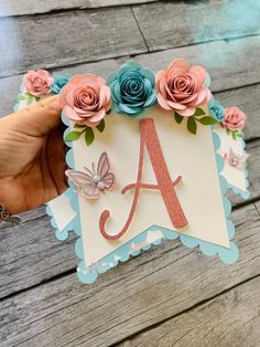 a hand holding up a card with flowers and a monogrammed letter on it