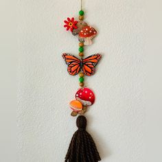 an orange butterfly hanging on a wall next to a mushroom and flower beaded necklace