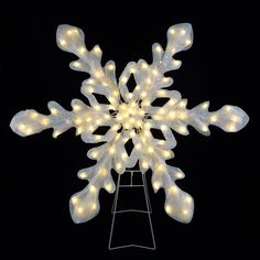 a lighted snowflake on a stand in the dark with lights all around it