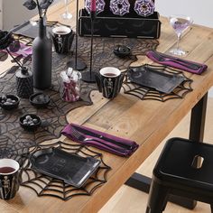 the table is set for halloween dinner with purple napkins and spider web place mats