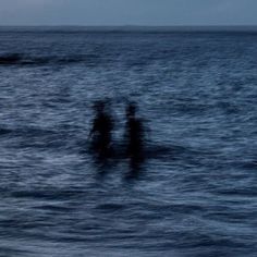 three people standing in the ocean at night with their backs turned to the camera,