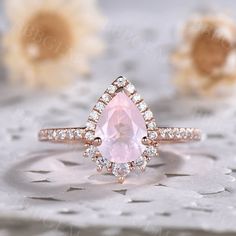 an engagement ring with a pear shaped morganite surrounded by smaller round diamonds on a lace tablecloth