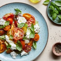 a blue plate topped with tomatoes and mozzarella cheese covered in herbs next to other ingredients