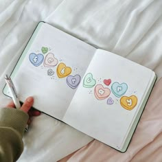 an open notebook with hearts drawn on it and a person holding a pen in their hand