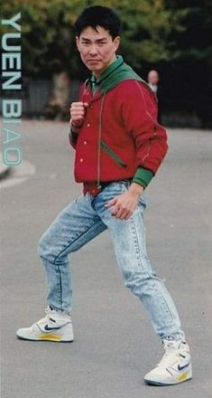 a young man walking across a parking lot wearing jeans and a red jacket with green trim