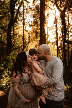 a man and woman holding their baby girl in the woods