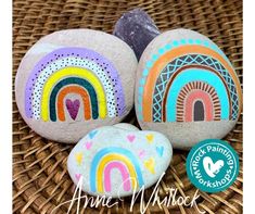 three painted rocks sitting on top of a wicker basket next to a rock with a rainbow