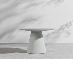 a white table sitting on top of a cement floor next to a wall with shadows