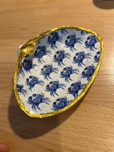 a blue and white crab dish sitting on top of a wooden table next to a person's hand