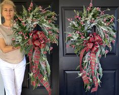 a woman standing in front of a black door holding two wreaths with red berries on them