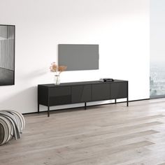 a living room with white walls and wooden floors, a black tv stand on top of a dresser next to a large window