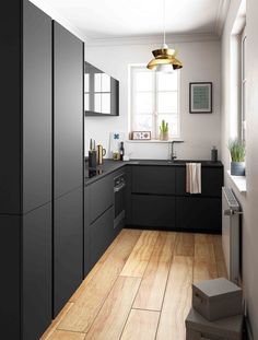 a kitchen with black cabinets and white walls, wood floors and a gold pendant light hanging over the sink