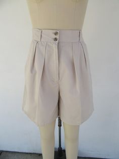 80s or maybe 90s high waist pleated khaki shorts. 65/35 poly cotton blend. Four pockets. Button detail on back. Super cute. Lightweight. Made  in Indonesia for 10 BROWING ST.  Label size 7/8 Please compare measurements to a similar garment that fits you well Measured flat 27" Waist 14" rise 40" hips 6-3/42" inseam   Good vintage condition with light signs of use and age. High Waist Vintage Shorts For Workwear, Vintage High Waist Shorts For Workwear, Vintage High-waist Shorts For Work, Vintage Shorts With Button Closure For Summer, Classic Summer Shorts With Button Closure, Vintage Workwear Shorts For Summer, High Waist Beige Shorts With Button Closure, Beige High Waist Shorts With Button Closure, Beige High-waisted Shorts With Button Closure