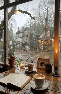 a cup of coffee sitting on top of a table next to a book and candle