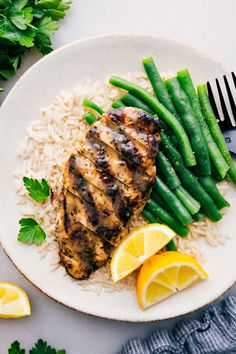 grilled chicken with rice, green beans and lemon wedges on a white plate