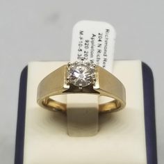 a yellow gold ring with a diamond on it sitting on top of a white box