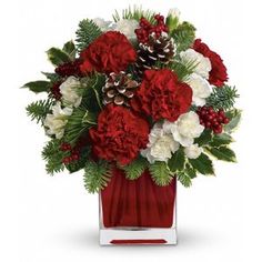 red and white flowers in a square vase with pine cones, holly branches and berries