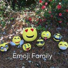 a group of smiley faces sitting on the ground next to some bushes and flowers with words emoji family