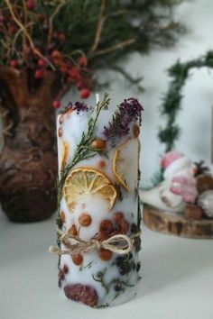 a candle that has been decorated with dried herbs and lemon slices on it, sitting next to a potted plant