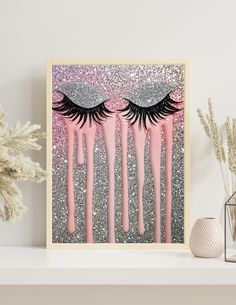 two eyelashes with pink and silver glitter on them are hanging from a shelf next to some flowers