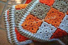 an orange and white crocheted blanket sitting on top of a wooden table next to a tile floor