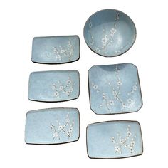 four blue dishes with white flowers on them and one has a branch in the middle