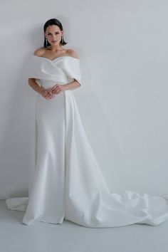 a woman in a white wedding dress standing against a wall with her hands on her hips