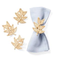 three napkins with gold leaves on them next to a blue bow tie and two napkin clips