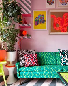 a colorful living room with pink walls and green couches, potted plants and pictures on the wall