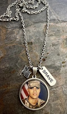 "This necklace is made on your choice of a 1\" or 3/4\" stainless steel pendant and includes two accent charms (flag and Brave charms). The chain is made with stainless steel that can be made in the length of your choice (24\", 26\", 28\", or 30\"). It can be made on a 3/4\" or 1\" pendant (default is 3/4\" unless noted otherwise in customer notes). INCLUDES: - Photo charm pendant - Brave charm - Flag charm - Options are available to purchase additional custom charms such as a photo, name, or da Navy Coast Guard, Air Force Gifts, Military Photos, Photo Charms, Memorial Necklace, Custom Charms, Photo Memories, Coast Guard, Stainless Steel Pendant