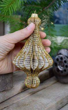 a hand holding a book page ornament in front of a christmas tree