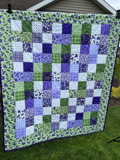 a green and purple quilt hanging from a clothes line on the grass in front of a house