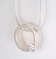 "This pendant is simple elegance.   It has been created from scratch using sterling silver and a cubic zirconia stone.  The stone has been set on top of a thick band of sterling silver.  The pendant hangs on a 1.5mm thick, 18\" long, snake chain.  The stone is available in pink or white/clear.  Please indicate your choice of color during check out in notes to seller. Weight: 15.8 grams, including chain and stone Dimensions: 7/8\" in diameter                          6mm wide                          2.5mm thick Please visit our shop to see the complimentary earrings. I am a full time jeweller and create all of my own designs and construct my work from scratch. I have been in business for over 10 years. I take pride in my designs and the quality of my craftsmanship. I pay very close attenti Modern Jewelry With Single Round-cut Diamond, Modern Jewelry With Single Round Cut Diamond, Modern Round Single Diamond Jewelry, Modern Single Diamond Jewelry In Diamond White, Modern Round Jewelry With Tension Setting, Sterling Silver Jewelry With Tension Setting Round Cut, Modern Sterling Silver Jewelry With Single Diamond, Modern Jewelry With Si Clarity Round Cut, Timeless Everyday Jewelry With Tension Setting