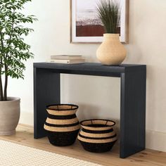 two black baskets sitting under a table next to a potted plant