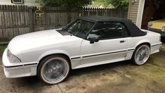 a white sports car parked in front of a house with a black top and chrome rims