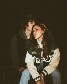 two people sitting on top of each other in front of a black background and one person with long hair