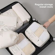 an open suitcase with several pieces of luggage in it and someone's hand on the lid