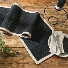 a place setting with black and white plates, napkins and silverware on a wooden table