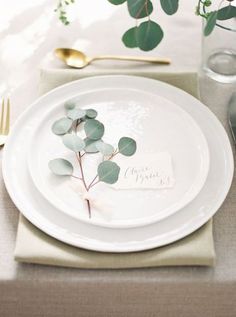 a place setting with white plates and greenery on the plate, along with silverware