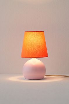 a white table lamp with a orange shade on it