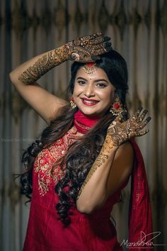 a woman with henna on her face and hands, smiling at the camera while wearing a red dress