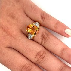 A vintage topaz and diamond ring, set in 18k solid yellow and white gold, containing a natural oval cut orange topaz. The ring contains round side diamonds with a cumulative weight of 0.30 carats. Total gram weight of the ring is 8.37 grams. A substantial semi-precious cocktail ring with excellent color contrast. The center stone is expertly cut, and bears maximum brilliance and color balance.   Item Details: - Type: Vintage Ring  - Metal: 18K Yellow, White Gold  - Weight: 8.37 Grams  - Setting: Luxury Oval Diamond Topaz Ring, Luxury Yellow Topaz Ring With Diamond Accents, Formal Orange Diamond Ring, Yellow Oval Diamond Ring, Fine Jewelry, Yellow Oval Diamond Ring Fine Jewelry, Fine Jewelry Yellow Oval Diamond Ring, Orange Diamond Ring With Center Stone, Classic Orange Diamond Ring, Orange Diamond Ring With Prong Setting