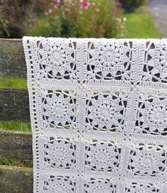 a white crocheted blanket hanging on a wooden fence in front of some flowers