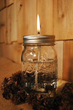 a mason jar with a lit candle in it sitting on a table next to pine cones