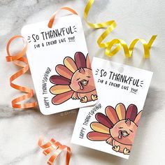 two tags with thanksgiving stickers on them next to orange ribbons and streamers that say thank you