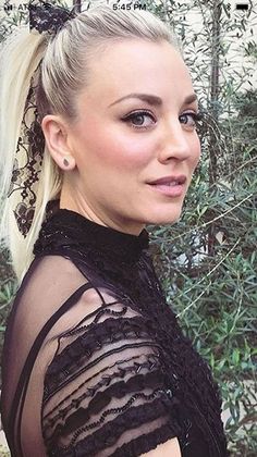 a woman with blonde hair wearing a black dress and headband in front of trees