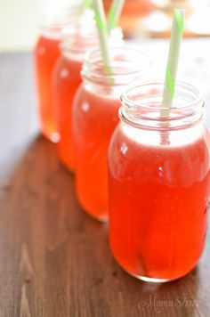 three mason jars filled with red liquid and green straws, sitting on a wooden table