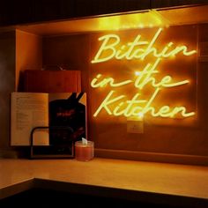 there is a neon sign that says bitchin in the kitchen next to an open book